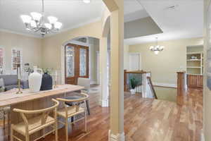 Dining space featuring a chandelier, arched walkways, french doors, wood finished floors, and ornamental molding