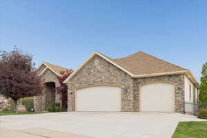 View of front of home with a garage, concrete driveway, stone siding, and a shingled roof