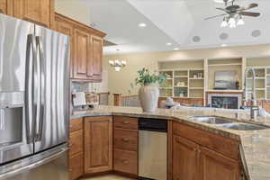 Kitchen featuring stainless steel refrigerator with ice dispenser, wood finish cabinets, a glass covered fireplace, open floor plan, and a chandelier