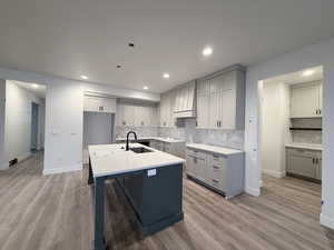 Kitchen with gray cabinets, a center island with sink, light wood finished floors, a breakfast bar, and recessed lighting