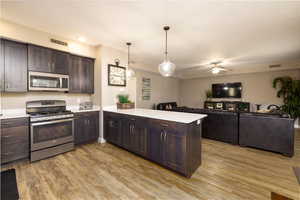 Kitchen with dark wood finish cabinetry, stainless steel appliances, a peninsula, light countertops, and open floor plan