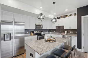 Kitchen featuring stainless steel appliances, a breakfast bar area, light stone counters, dark wood-type flooring, and a kitchen island