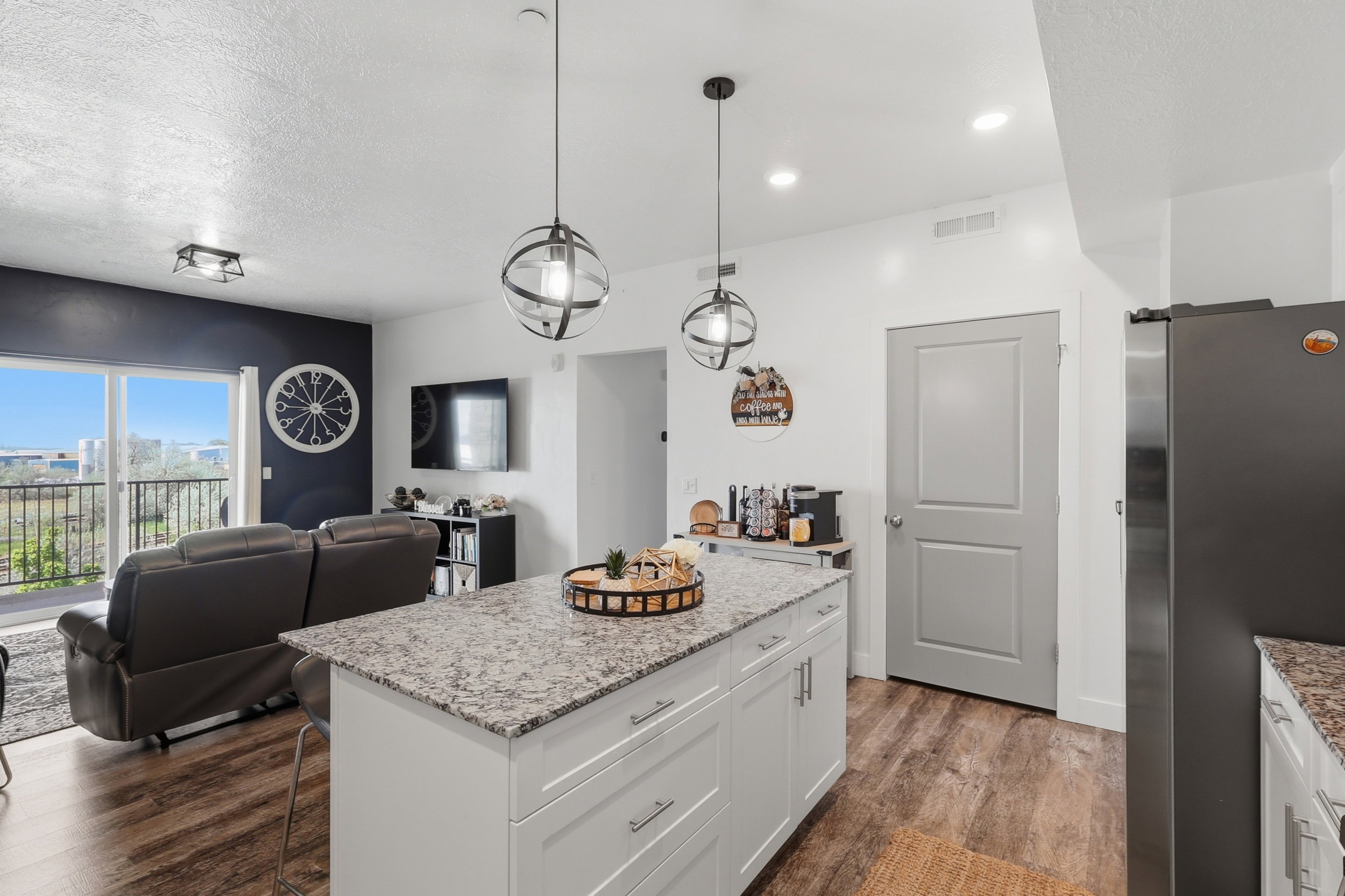 Kitchen with freestanding refrigerator, light stone counters, white cabinets, open floor plan, and dark wood-style flooring