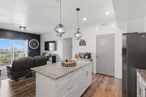 Kitchen with freestanding refrigerator, light stone counters, white cabinets, open floor plan, and dark wood-style flooring