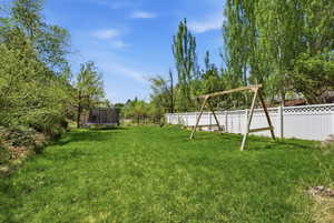 Fenced backyard with a trampoline and view of scattered trees