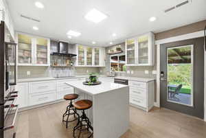 Kitchen featuring glass fronted cabinets, open shelves, a kitchen bar, a center island, and recessed lighting