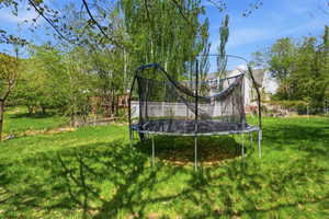 Fenced backyard featuring a trampoline and view of wooded area