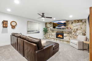 Living room with carpet, ceiling fan, a stone fireplace, and recessed lighting