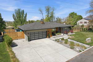 View of front of home with concrete driveway, a chimney, roof with shingles, and an attached garage