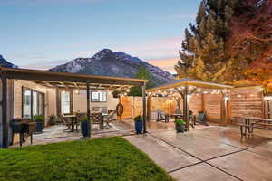 Patio terrace at dusk with grilling area, a patio area, outdoor dining space, a fenced backyard, and a mountain view