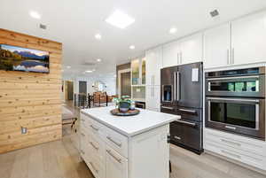 Kitchen with white cabinetry, double oven, high end fridge, a center island, and recessed lighting
