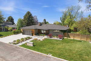 Ranch-style home with a front yard, an attached garage, concrete driveway, a chimney, and brick siding