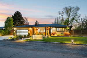 View of front of home featuring a garage, driveway, brick siding, and a chimney
