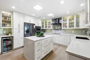 Kitchen featuring glass insert cabinets, light stone counters, beverage cooler, white cabinets, and recessed lighting