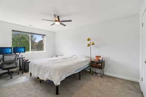 Carpeted bedroom with an office area and ceiling fan
