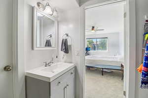 Ensuite bathroom with vanity, light colored carpet, and a ceiling fan