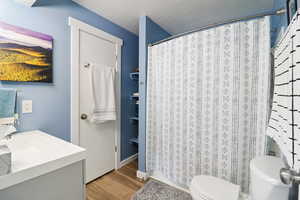 Full bathroom with vanity, light wood-style floors, a shower with shower curtain, and a textured ceiling