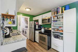 Kitchen featuring stainless steel appliances, white cabinets, open shelves, separate washer and dryer, and light wood-style flooring