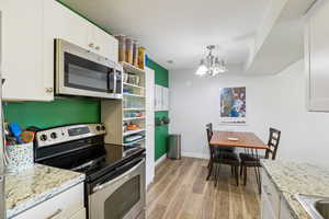 Kitchen with stainless steel appliances, white cabinets, and suspended lighting