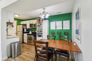Kitchen with stainless steel appliances, suspended lighting, light wood-style floors, white cabinetry, and open shelves