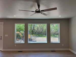 Empty room with a textured ceiling, light wood-style flooring, ceiling fan, recessed lighting, and healthy amount of natural light