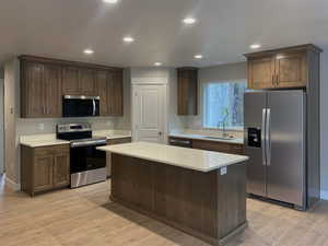 Kitchen with stainless steel appliances, recessed lighting, a center island, light wood-style floors, and light stone counters