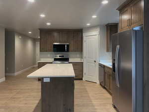 Kitchen featuring stainless steel appliances, recessed lighting, light wood-type flooring, a kitchen island, and light stone counters
