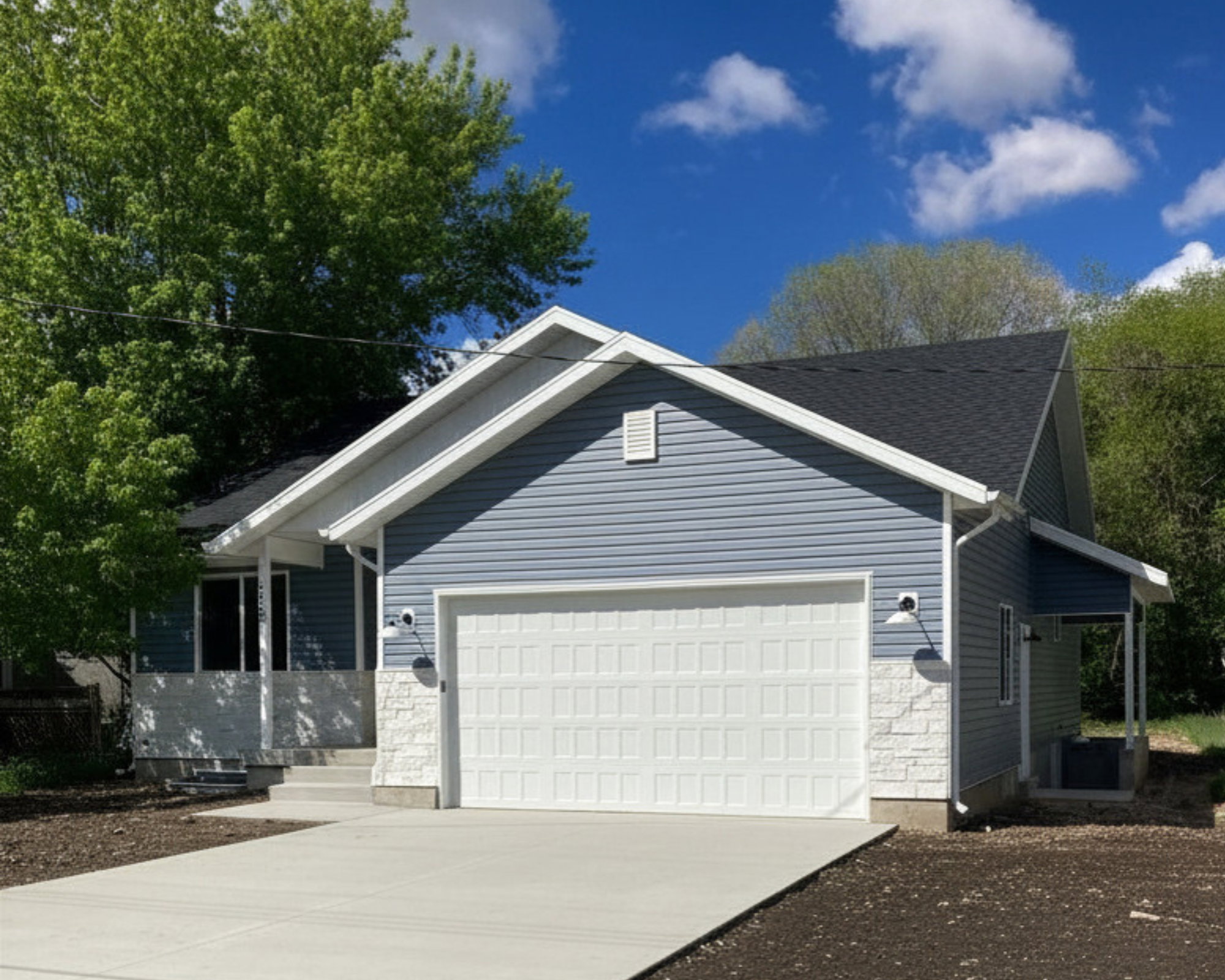 Exterior featuring light blue horizontal siding, white garage door, and stone facade accents