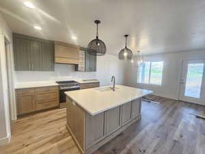 Dual tone kitchen featuring stainless steel gas range oven, a kitchen island with sink, pendant lighting, light wood finished floors, and dual tone cabinetry