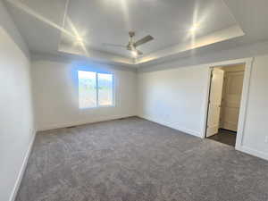 Unfurnished bedroom with ceiling fan, dark colored carpet, and a tray ceiling