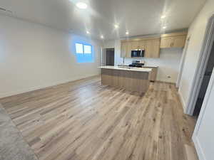 Kitchen featuring light wood-style floors, a center island with sink, recessed lighting, stainless steel appliances, and open floor plan