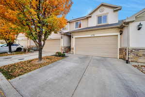 View of front of home with stone siding, driveway, an attached garage, and stucco siding