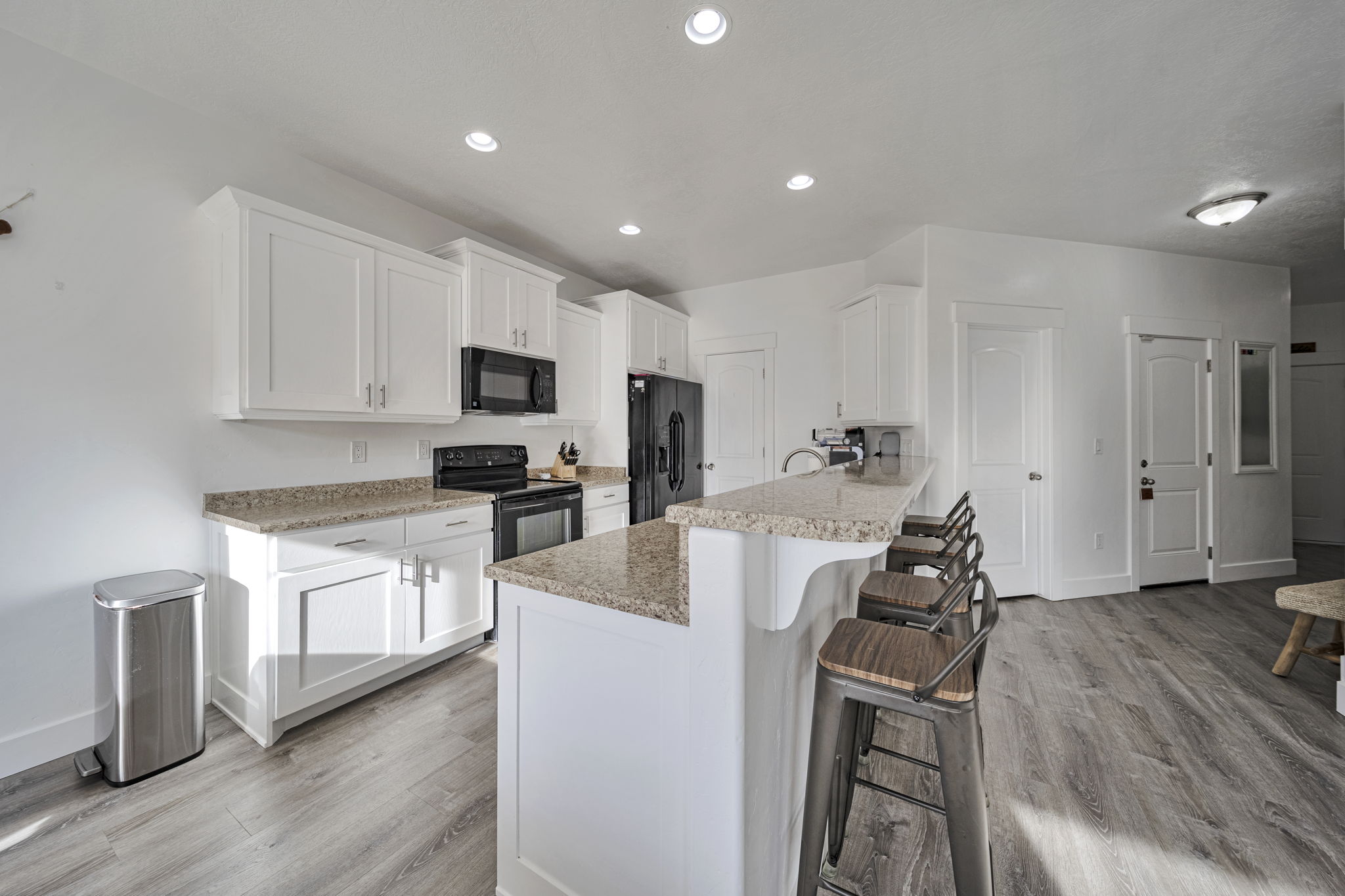Kitchen with white cabinetry, a breakfast bar, black appliances, light wood-style flooring, and a peninsula