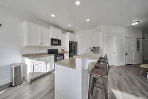 Kitchen with white cabinetry, a breakfast bar, black appliances, light wood-style flooring, and a peninsula