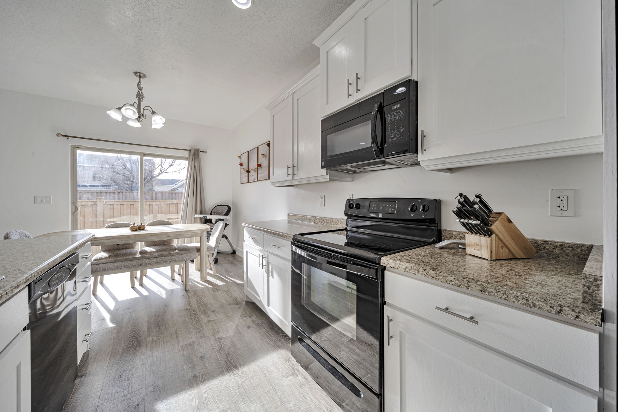Kitchen with black appliances, white cabinetry, suspended lighting, and light wood-style floors