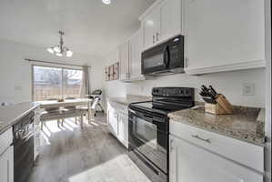 Kitchen with black appliances, white cabinetry, suspended lighting, and light wood-style floors