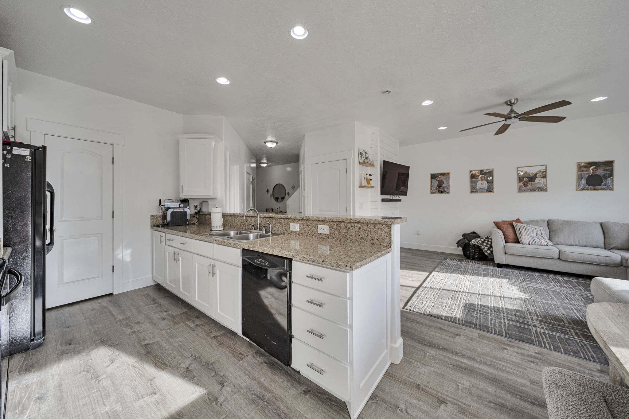 Kitchen featuring a peninsula, white cabinetry, open floor plan, light stone countertops, and light wood-style flooring