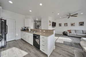 Kitchen featuring a peninsula, white cabinetry, open floor plan, light stone countertops, and light wood-style flooring