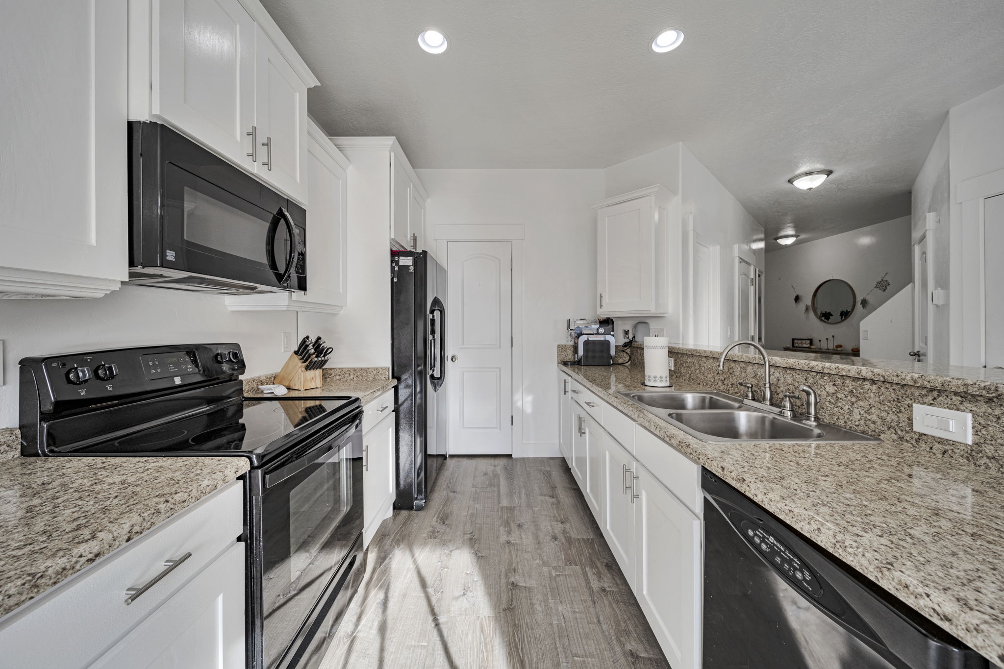 Kitchen featuring black appliances, white cabinetry, and light stone countertops