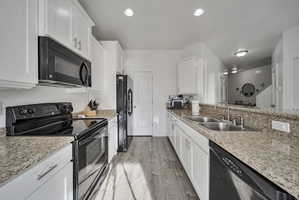 Kitchen featuring black appliances, white cabinetry, and light stone countertops