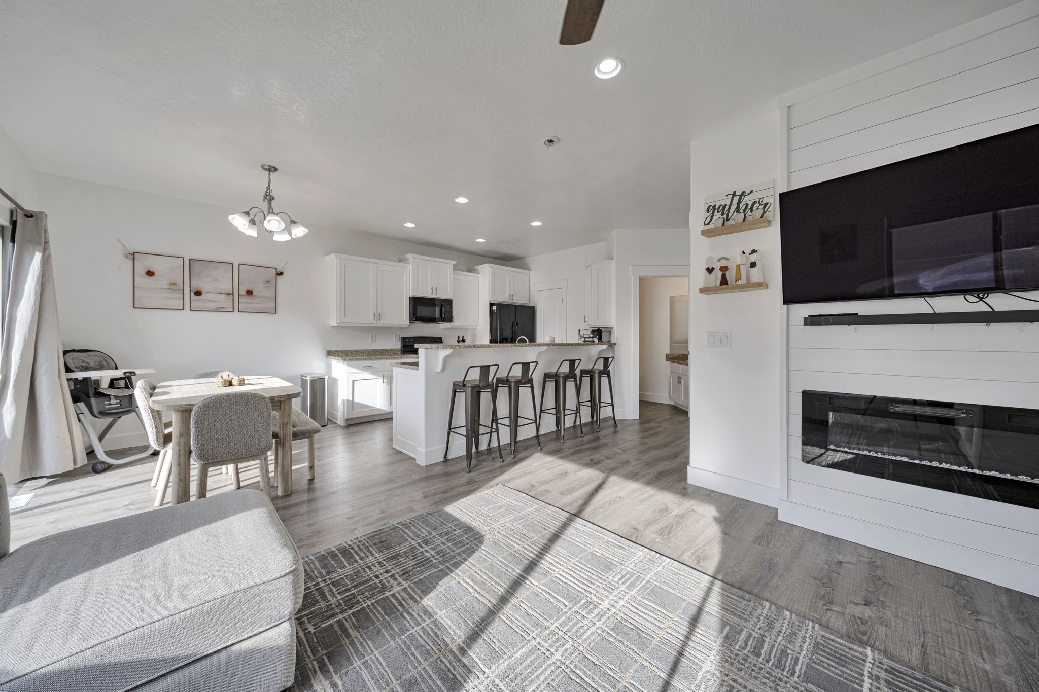 Living room featuring light wood-style floors, a chandelier, ceiling fan, and a glass covered fireplace