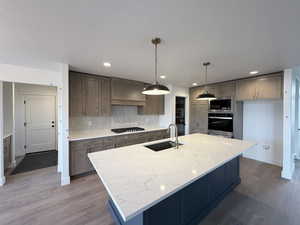 Kitchen featuring light stone counters, stainless steel appliances, dark wood-style floors, decorative light fixtures, and a center island with sink