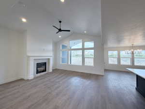 Unfurnished living room featuring dark wood-style floors, a tiled fireplace, suspended lighting, ceiling fan, and a high ceiling