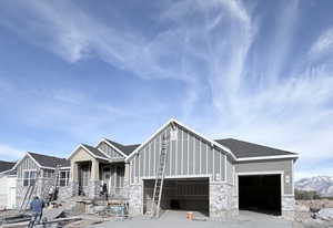 View of front facade featuring an attached garage, stone siding, and a shingled roof