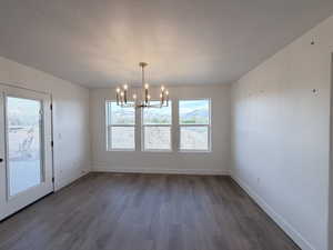 Unfurnished dining area with hanging lights, dark wood-style floors, and a textured ceiling
