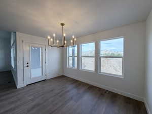 Unfurnished dining area featuring hanging lights, dark wood-type flooring, and a textured ceiling