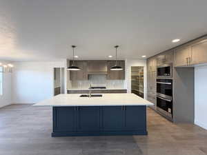 Kitchen featuring light stone countertops, hanging light fixtures, light wood-type flooring, a kitchen island with sink, and stainless steel appliances