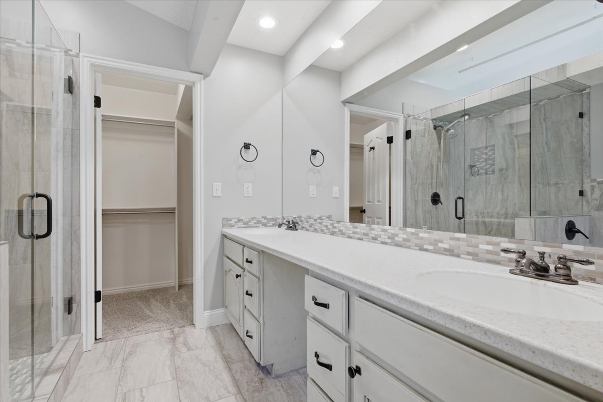 Bathroom featuring a shower stall, double vanity, a walk in closet, tasteful backsplash, and light marble finish flooring