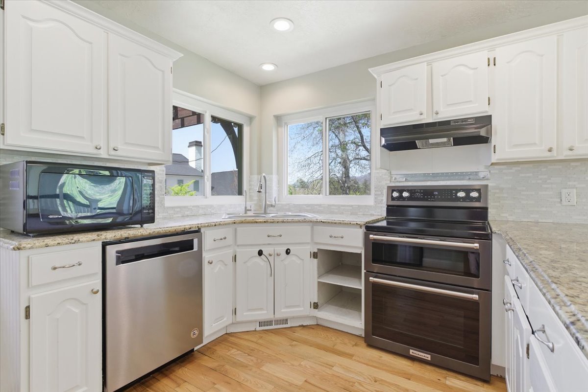 Kitchen featuring stainless steel appliances, white cabinetry, light wood-type flooring, light stone counters, and recessed lighting