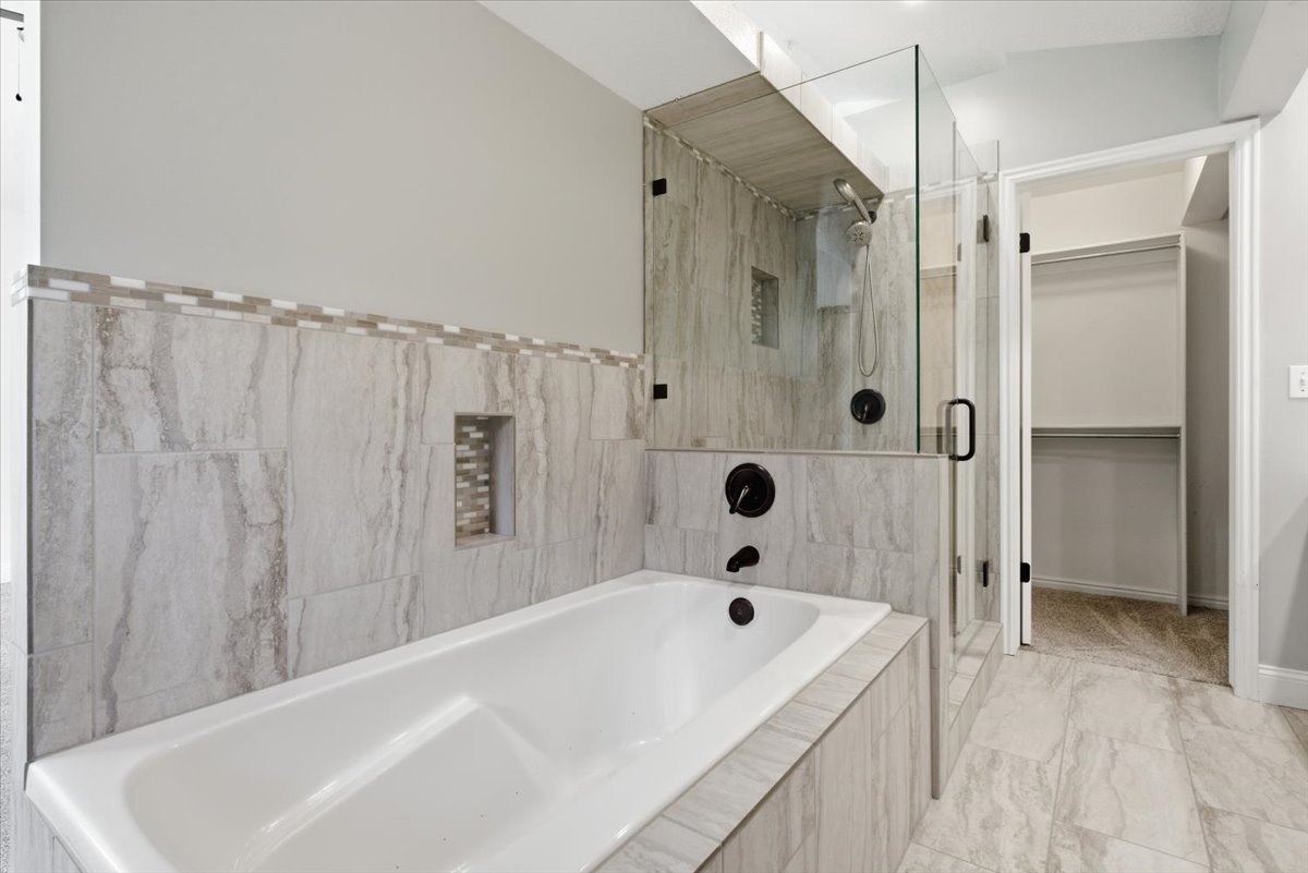 Full bathroom featuring a shower stall, a bath, and a spacious closet